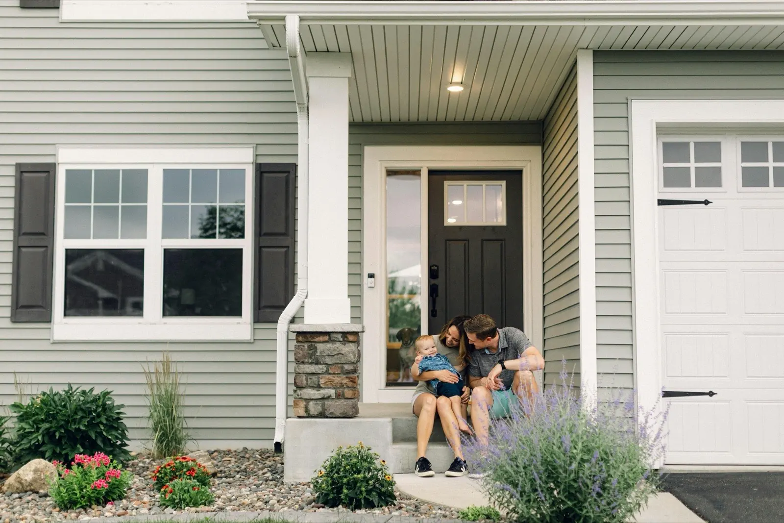 A young family sitting together on the front steps of their new home on a summer evening